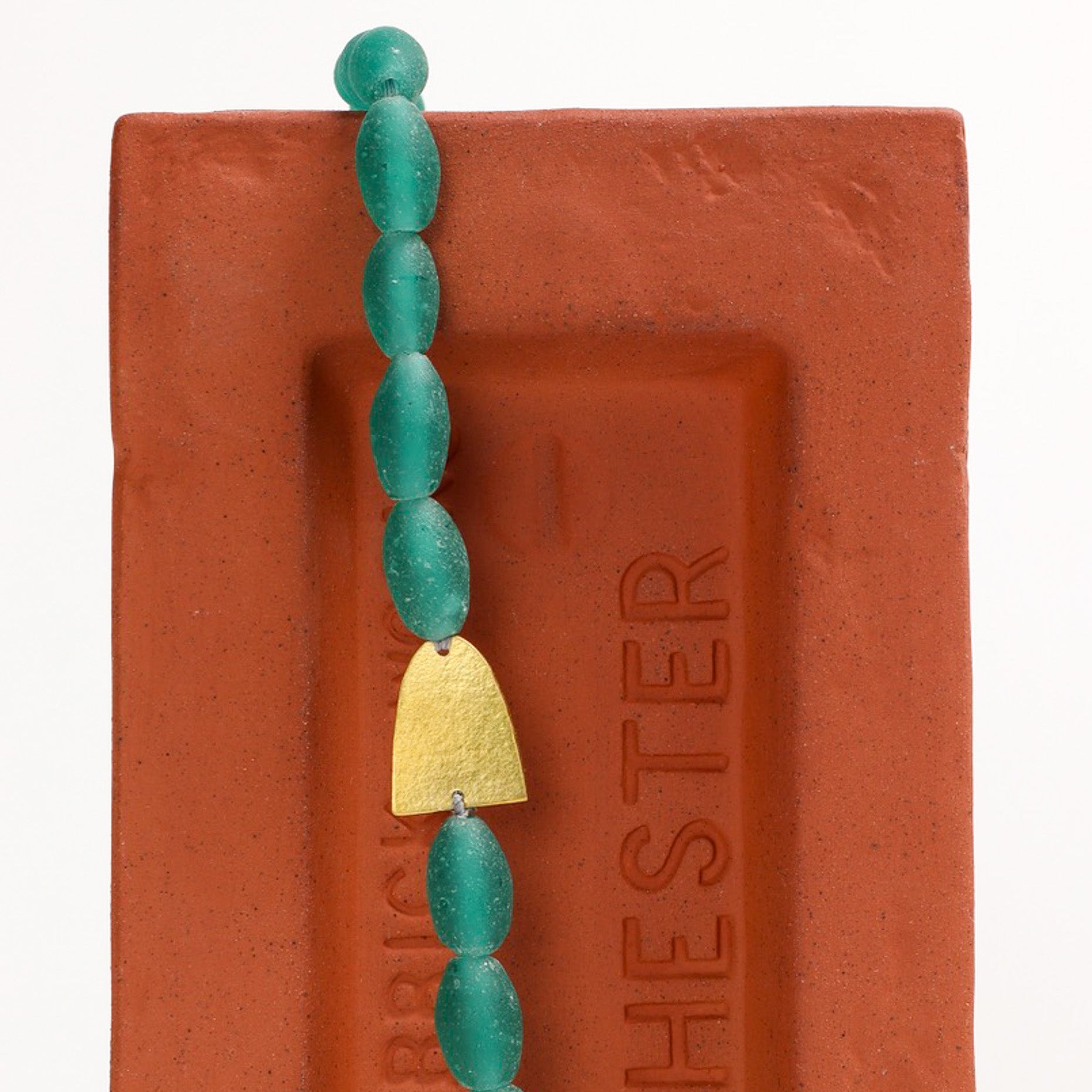 Green beaded necklace with brass detail on a brick background