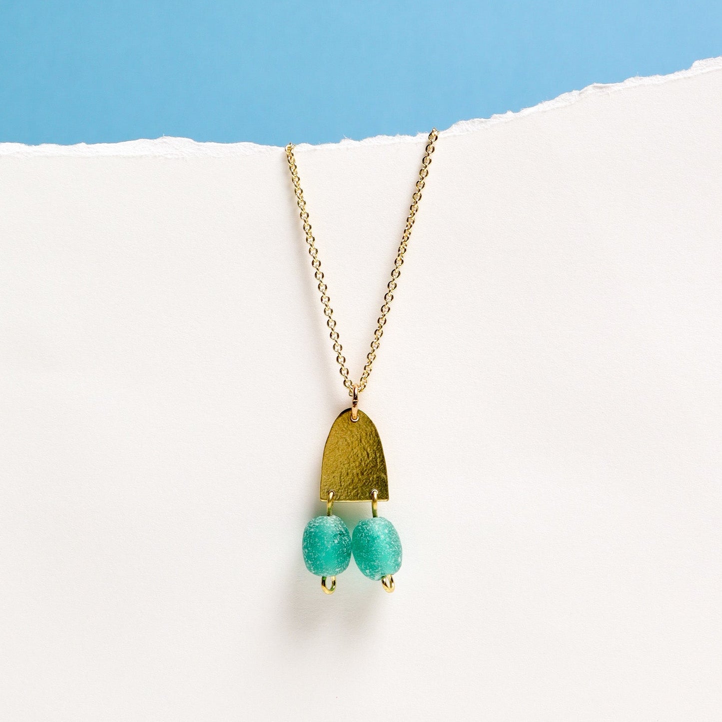 Necklace with a gold pendant and turquoise beads on a white surface with a blue background