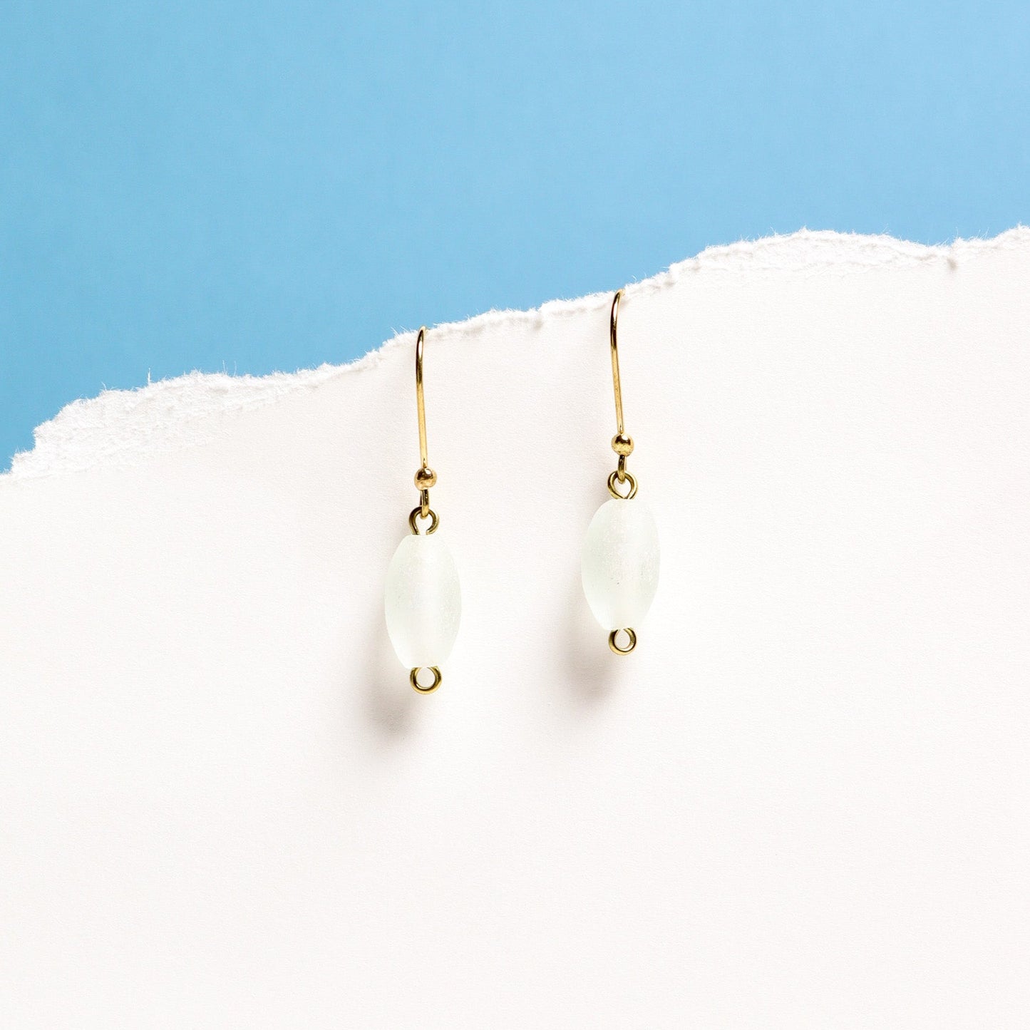 Gold earrings with white stones on a white surface with a blue background