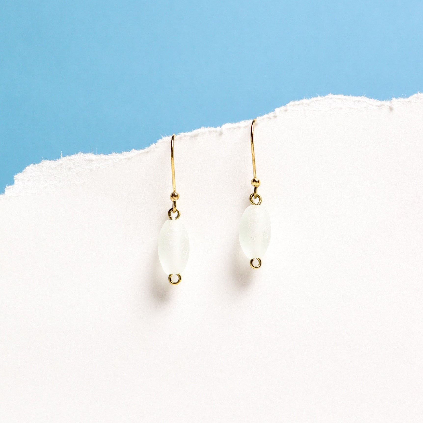 Gold earrings with white stones on a white surface with a blue background