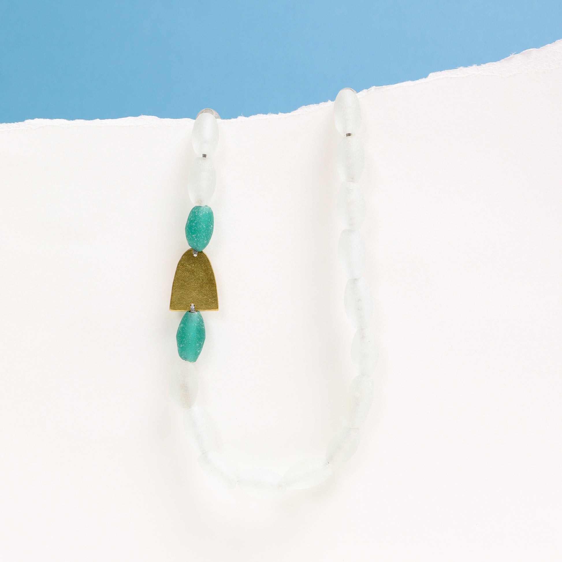 Necklace with turquoise and gold pendant on a white surface with blue background