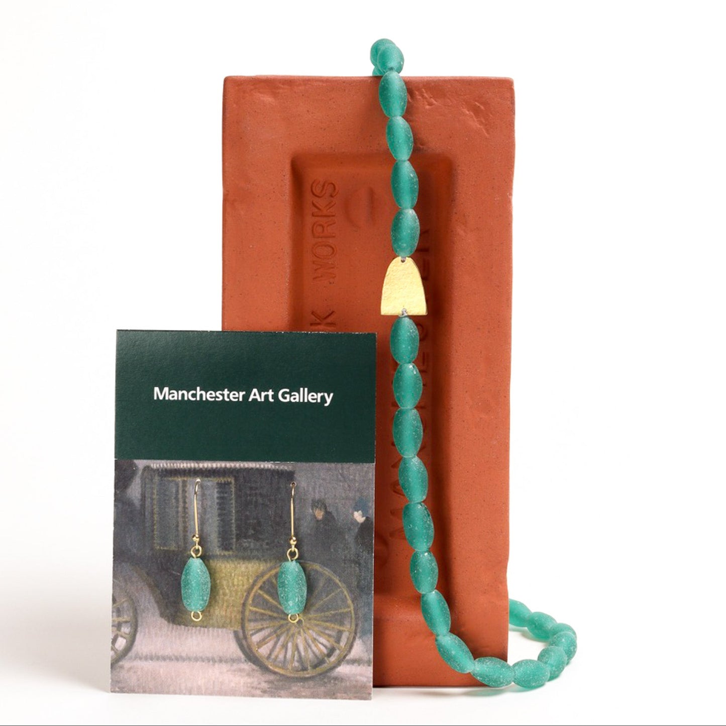 Turquoise beaded necklace with matching earrings displayed on a Manchester Art Gallery card and a brown brick.