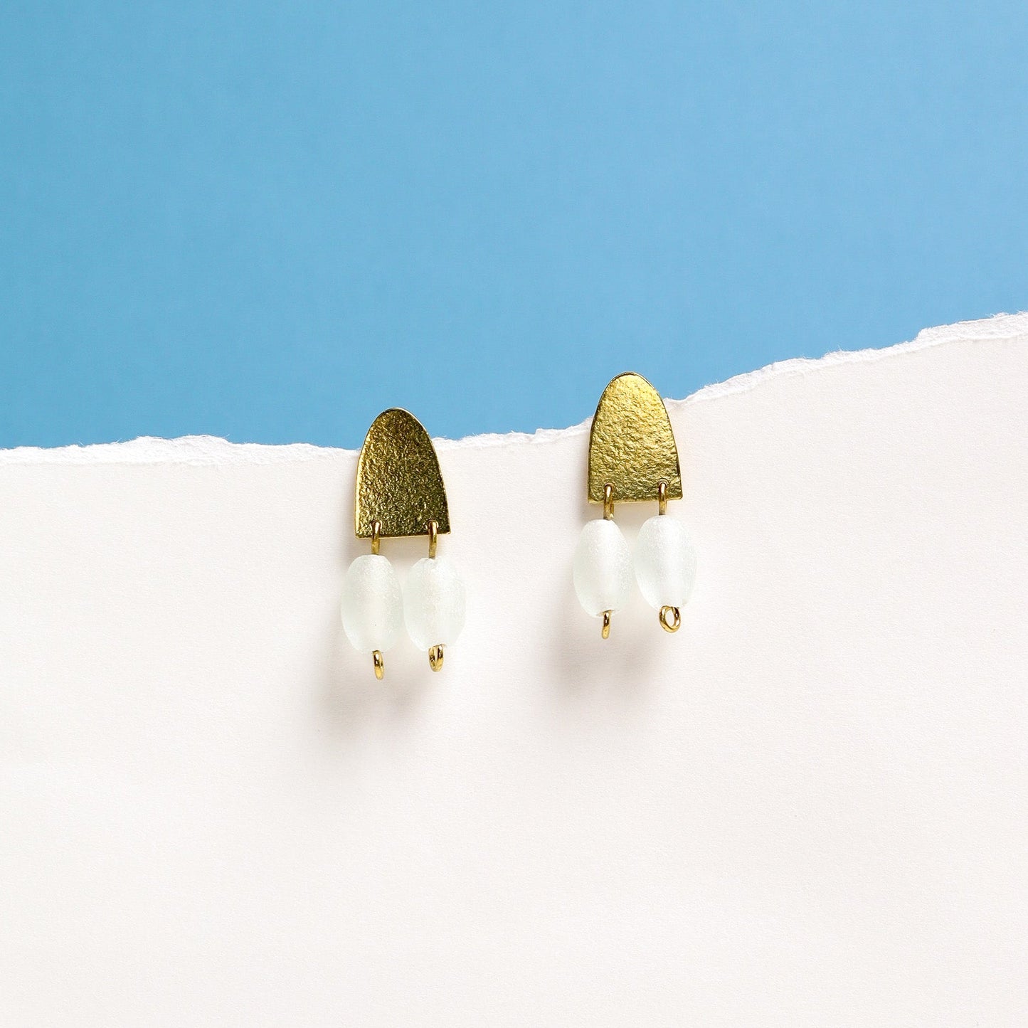 Gold and white bead earrings on a white surface with a blue background
