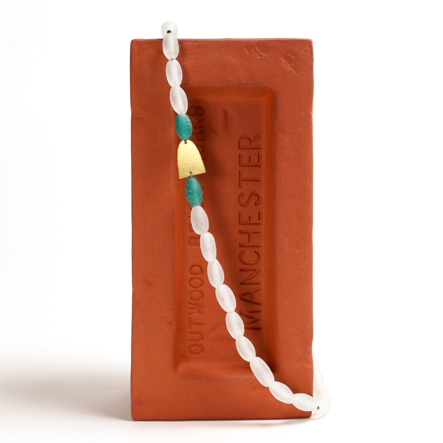 Necklace with white and blue beads displayed on a red brick with 'Manchester' branding.