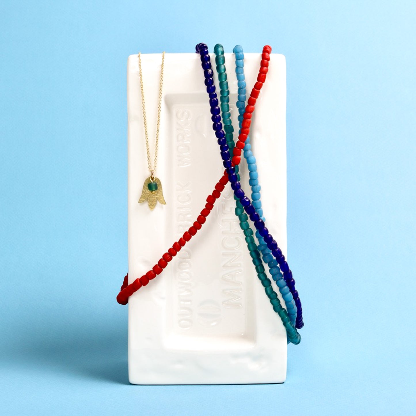 Set of beaded necklaces on a white brick against a blue background