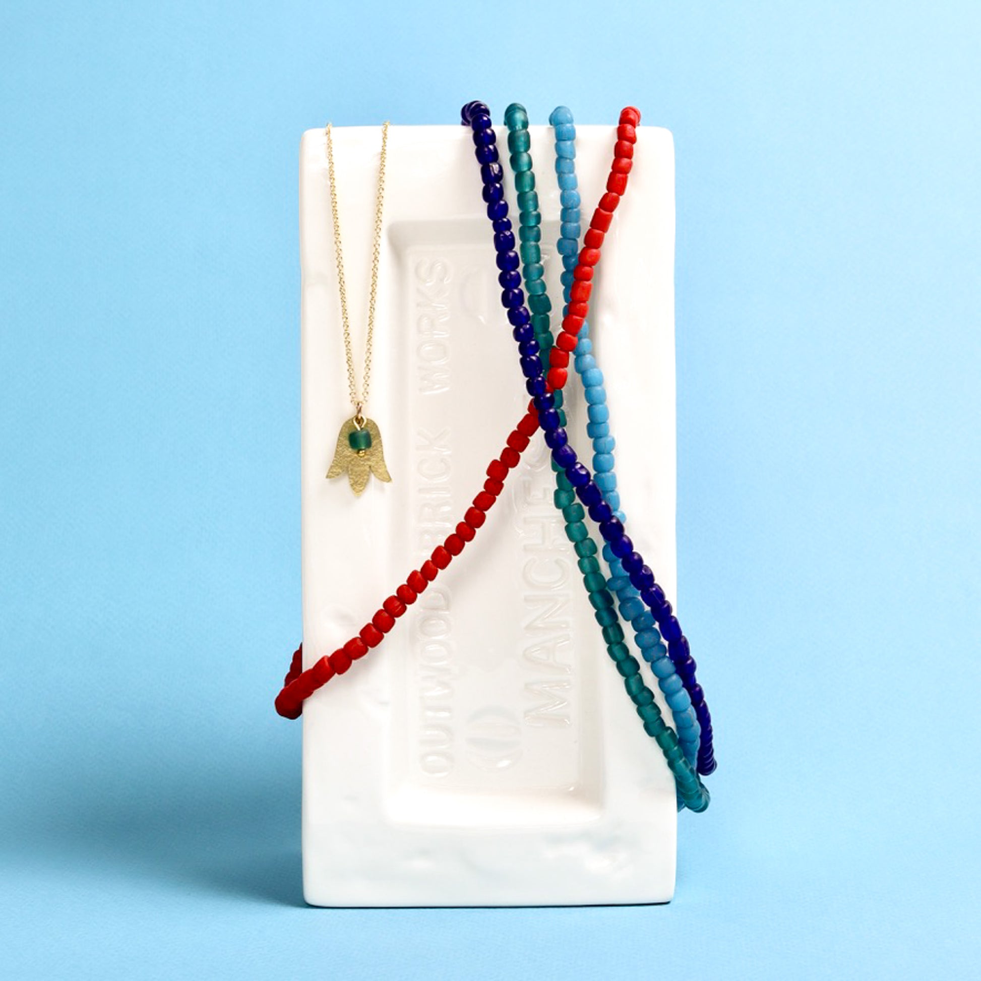 Set of beaded necklaces on a white brick against a blue background
