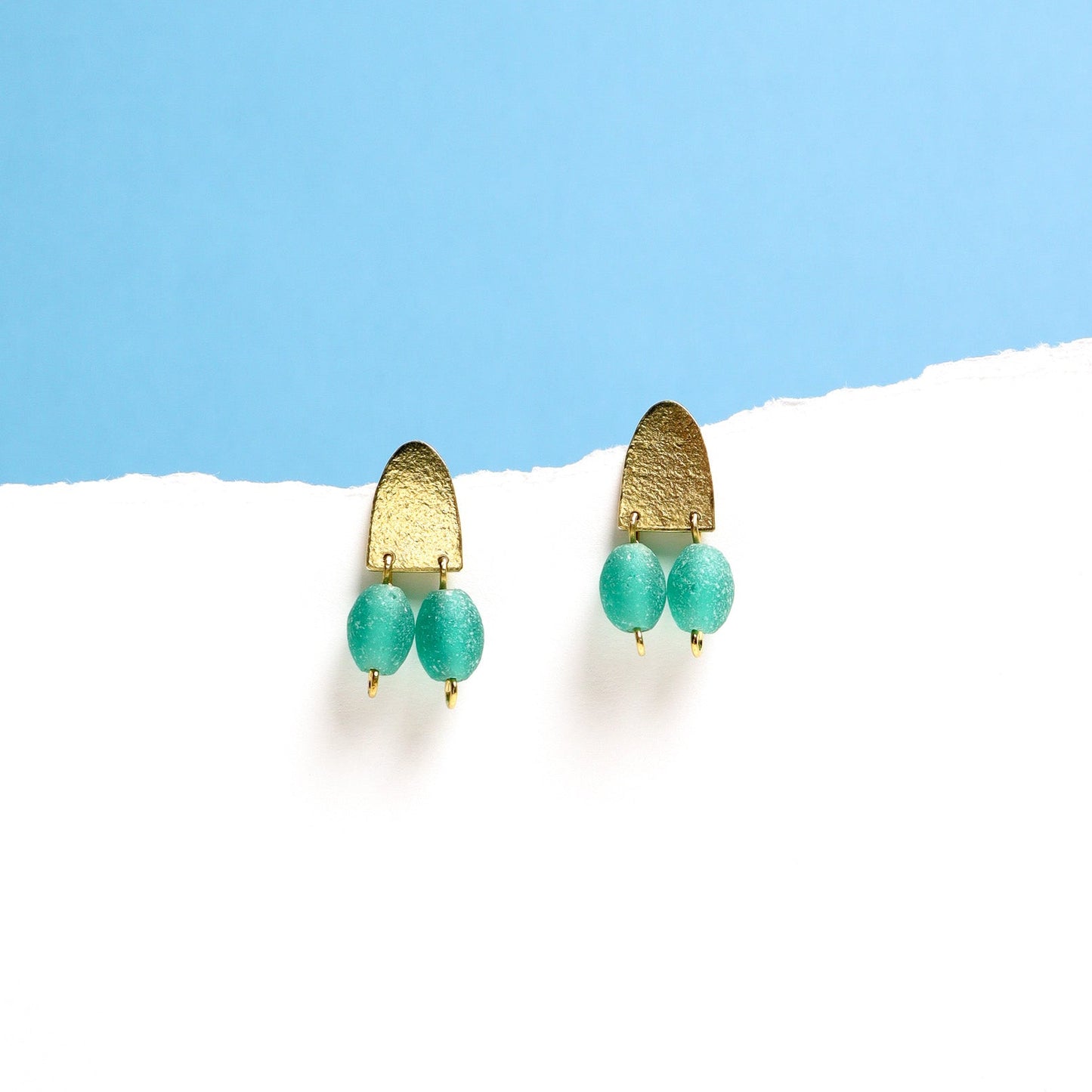 Brass earrings with teal green beads on a white and blue background