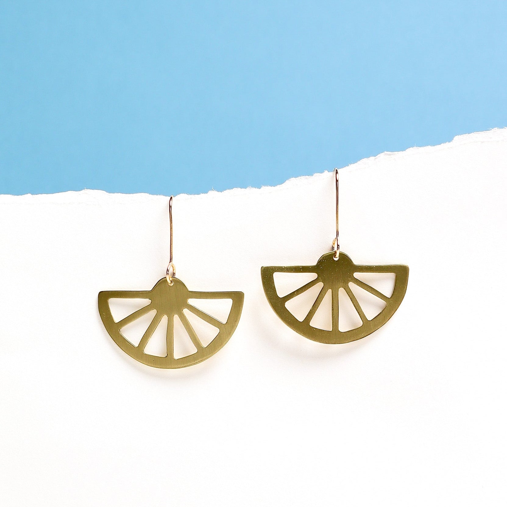 Gold earrings with a wagon wheel design on a white surface with a blue background