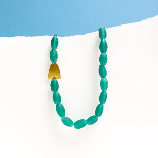Green beaded necklace with a gold accent on a white surface with blue background
