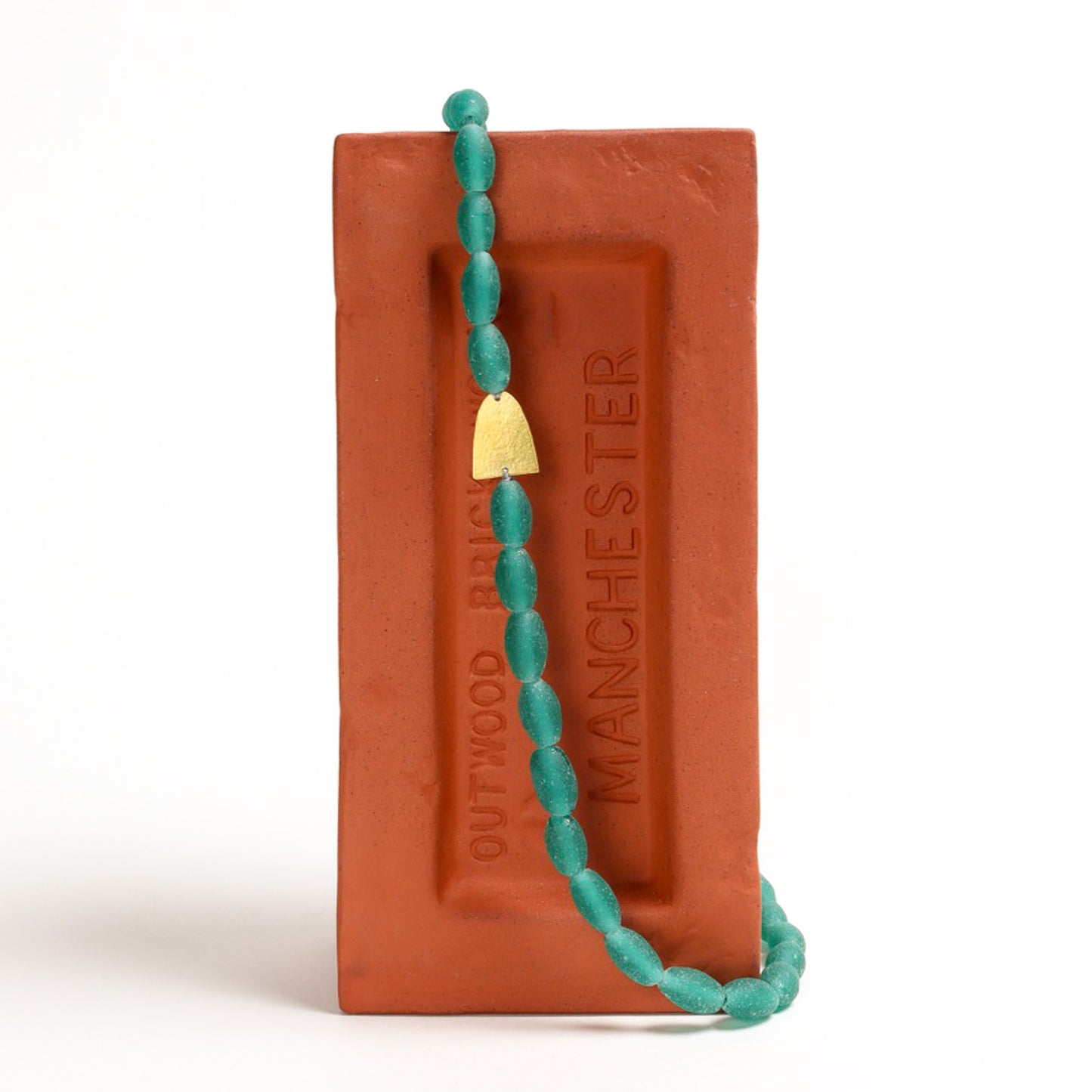 Turquoise beaded necklace displayed on a red brick with 'Manchester' branding.