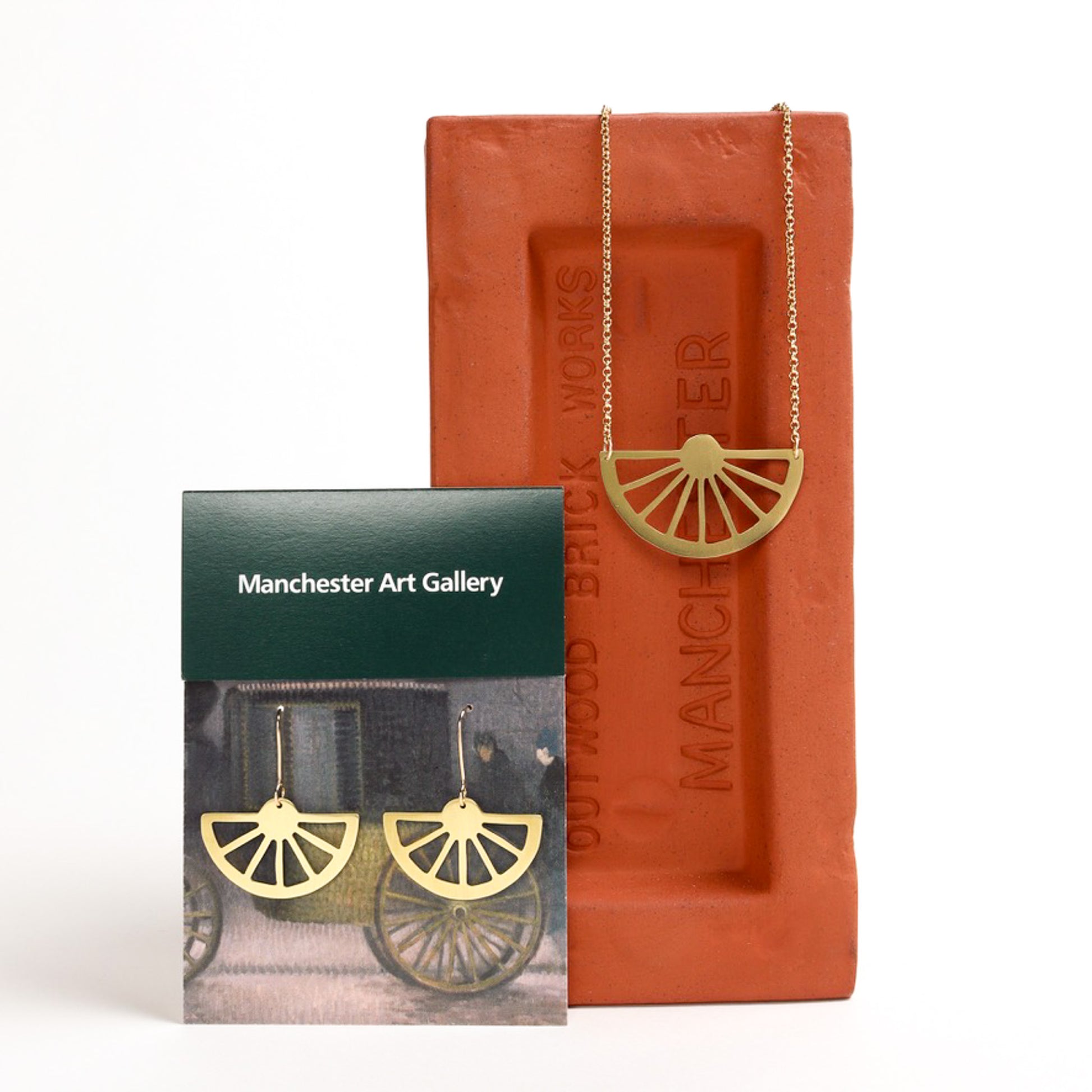 Brass wagon wheel pendant and earrings with 'Manchester Art Gallery' packaging on a white background