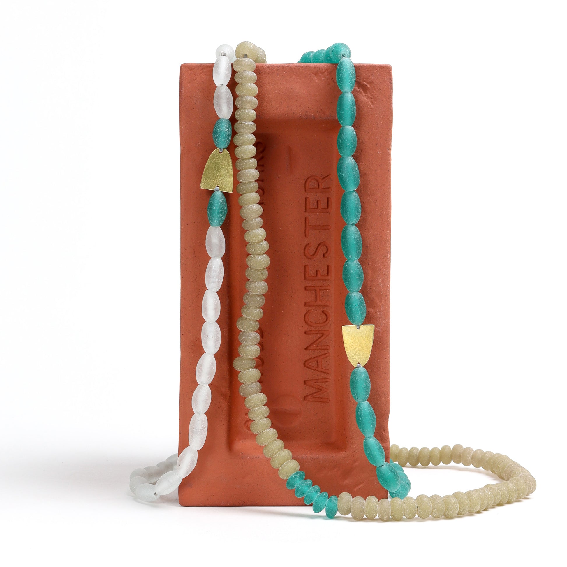 collection of necklaces with turquoise, white and beige beads on a red brick with 'Manchester' branding.