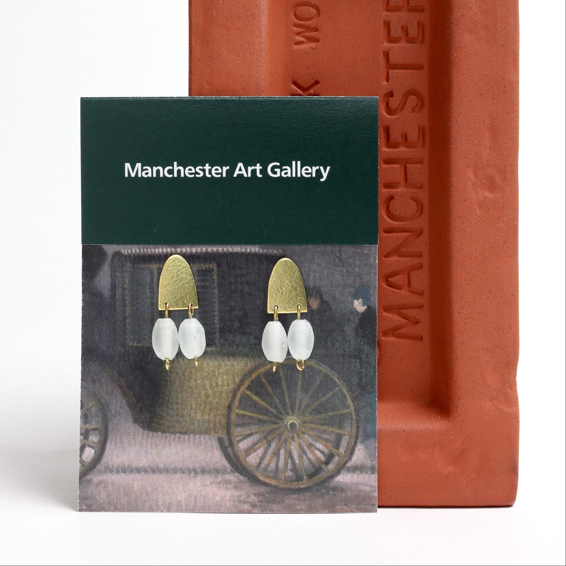 Earring packaging with 'Manchester Art Gallery' branding next to a brick.