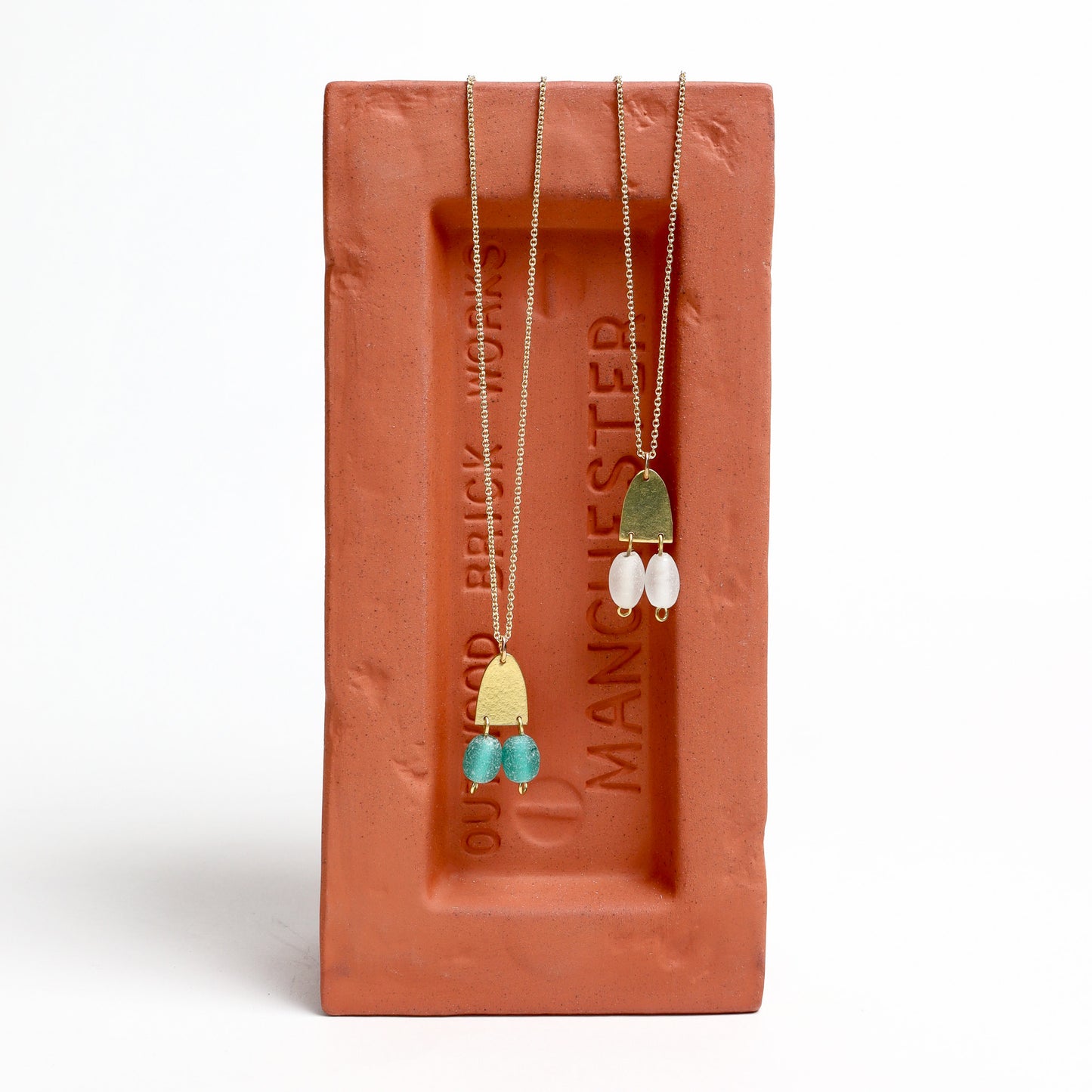 Two brass pendents set on a brick-shaped stand with 'Brickworks by Manchester' branding.