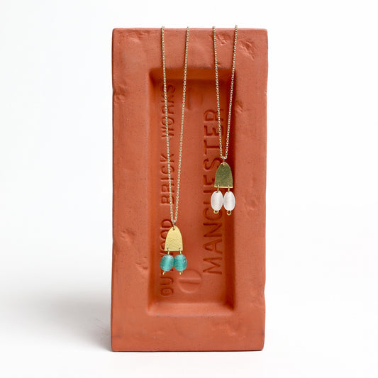 Two brass pendents set on a brick-shaped stand with 'Brickworks by Manchester' branding.