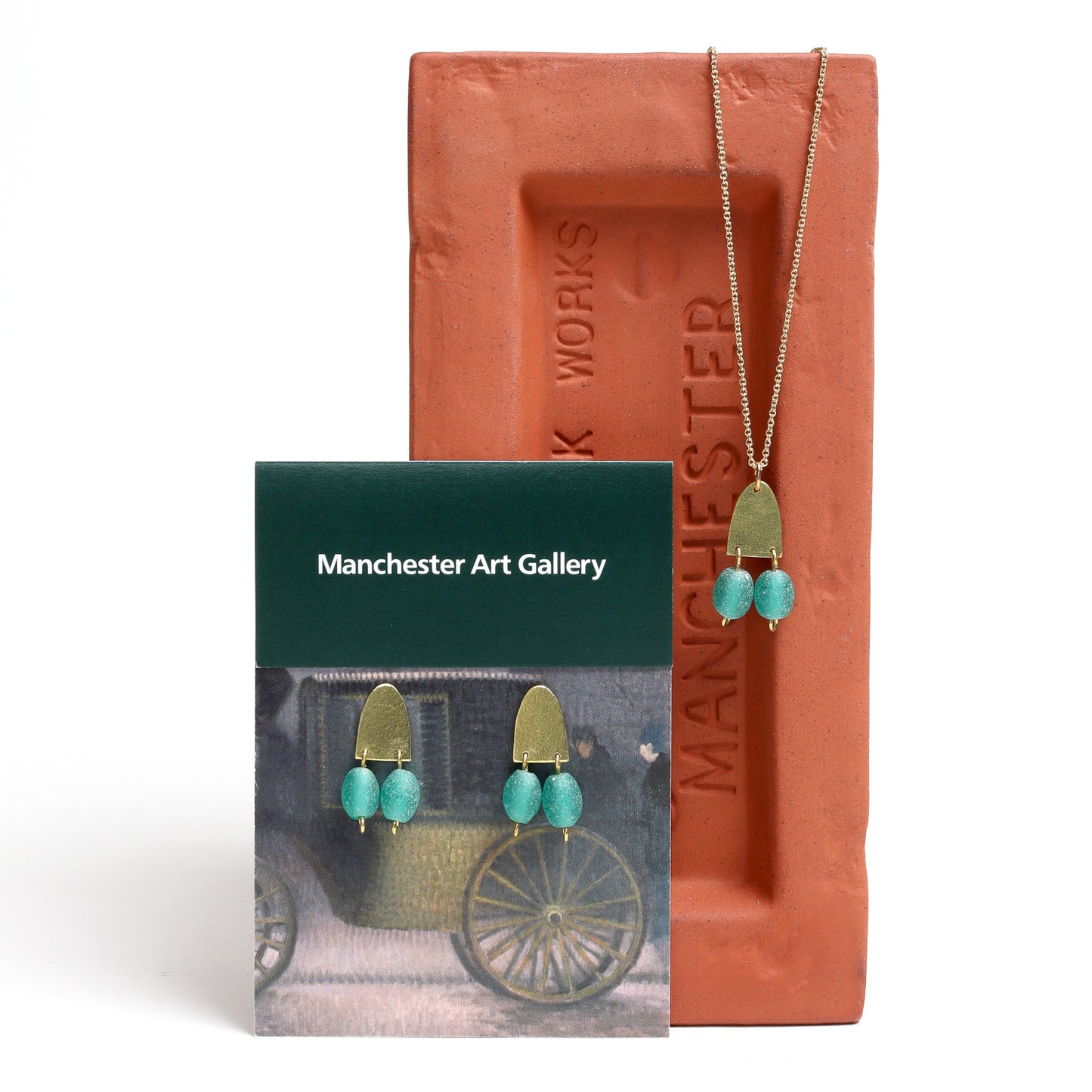 Jewelry set with turquoise stones and gold accents, including earrings and a necklace, displayed against a Manchester Art Gallery card.