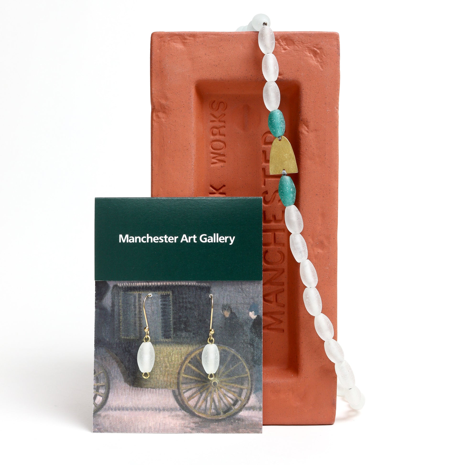 Necklace and earring set with white and blue beads displayed on a red brick with 'Manchester' branding.