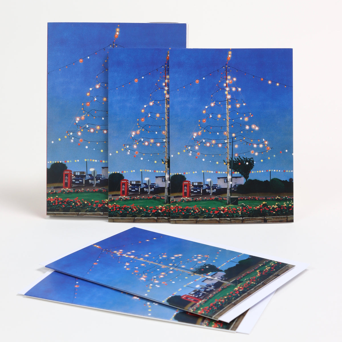 A set of greetings cards photographed of a white background. Each card features the artwork Celebration by Ray Smith. The image is of a blue night sky with a fairy lights suspended in the shape of a Christmas tree.