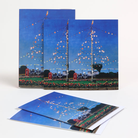 A set of greetings cards photographed of a white background. Each card features the artwork Celebration by Ray Smith. The image is of a blue night sky with a fairy lights suspended in the shape of a Christmas tree.