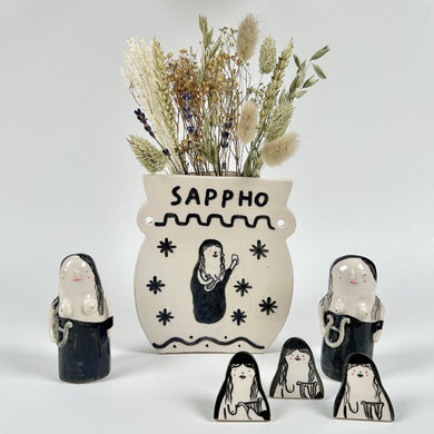 Image of the Alex Sickling bud vase surrounded by the Alex Sickling Sappho figurine  and pin badge 